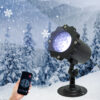 Adjustable base snowflake projection light, hand holding wireless remote control to operate lamp, snowy pine forest winter backdrop with floating white snowflake patterns, outdoor holiday decorative light product shot