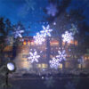 Black outdoor snowflake projection light at night, projecting large white snowflake patterns onto brick villa exterior walls and trees, dark blue evening sky background, winter Christmas decorative lamp effect display image