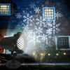 Outdoor wall-mounted snowflake projection light showcasing bright white snowflake patterns projected onto dark brick villa exterior at night, garden string lights and green shrubs in foreground, winter holiday yard decor demo image