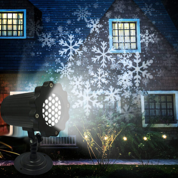 Outdoor wall-mounted snowflake projection light showcasing bright white snowflake patterns projected onto dark brick villa exterior at night, garden string lights and green shrubs in foreground, winter holiday yard decor demo image